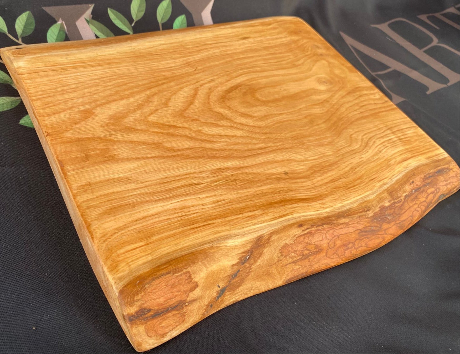 Wooden cutting board on a black surface with green leaves